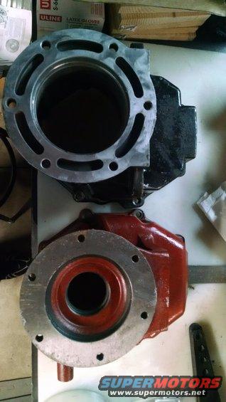 Engine block and cylinder head parts on a table. The cylinder head is silver with a large circular opening. The engine block is red and black with a circular flange
