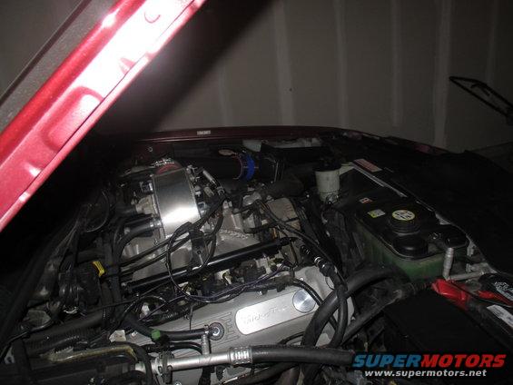 Ford V8 engine bay with silver valve covers and blue air intake hose