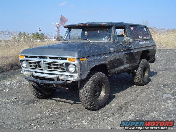Ford Bronco with big tires and a custom bumper, parked on a dirt road