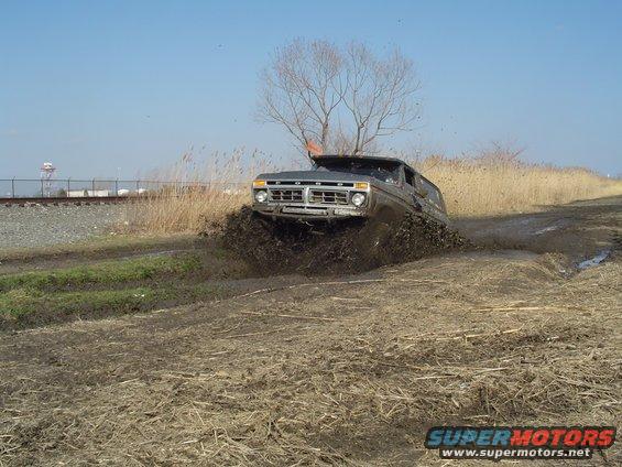 Dark gray 1978 Ford Bronco driving through mud, front grille visible