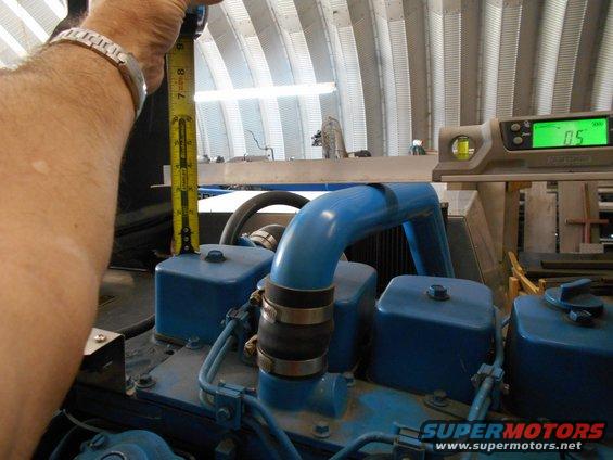 hand holding tape measure over blue engine component, digital level shows 0.5