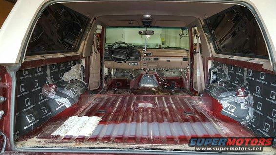 Interior of a stripped-down SUV, showing bare metal floor and sound deadening on the doors