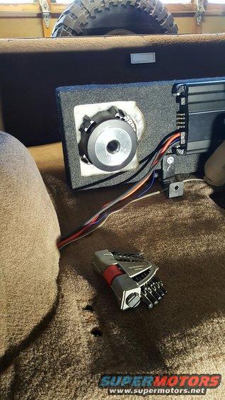 Car interior with speaker, amplifier, and tools on carpet. Spare tire visible