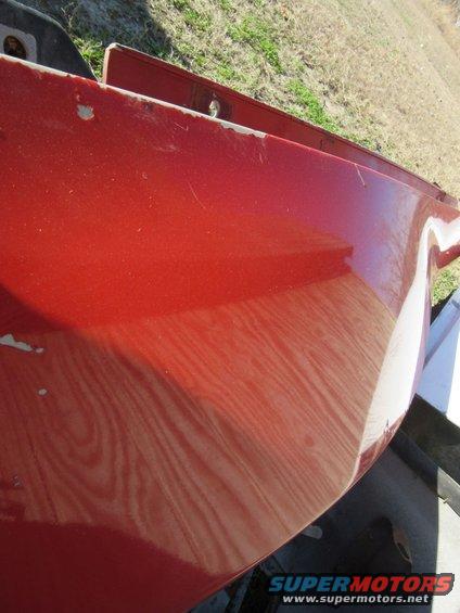 Close-up of a red car fender with visible scratches and paint chips