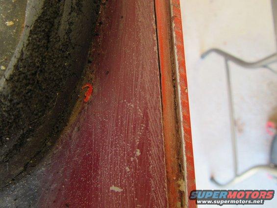 Close-up of red painted metal with dirt and a small orange piece, showing a seam and some dust