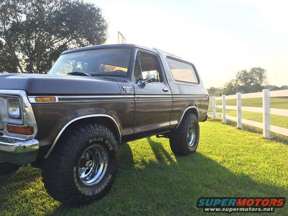 1978 Ford Bronco parked on grass next to a white fence