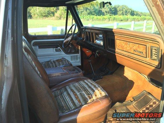 Interior view of a 1978 Ford Bronco showing worn striped cloth and brown vinyl seats, dashboard with woodgrain trim, and floor mats