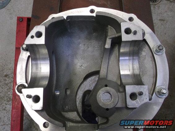 Close-up of an open differential housing with internal gears visible. The part is mounted on a red stand