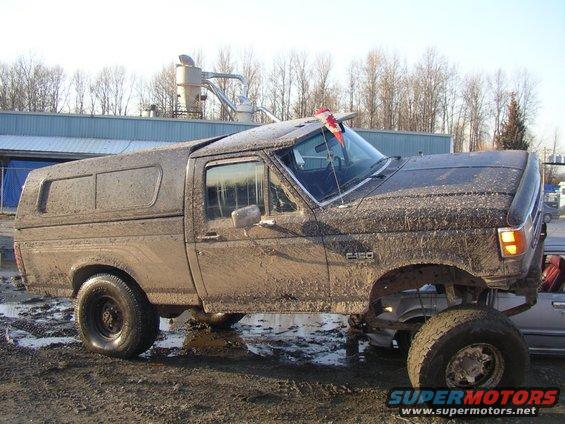 Muddy 1990 Ford F-150 with a camper shell and a Canadian flag on the visor