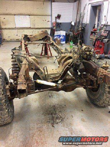 rusted vehicle frame with engine and suspension components in a garage