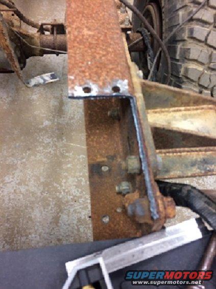 Rusted metal frame section with visible welds and bolts, part of a tire in the background