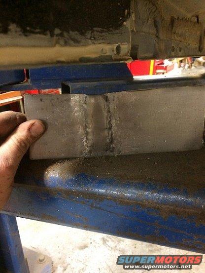 hand holding a welded metal bracket against a vehicle frame on a lift