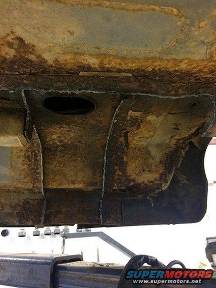 Heavily rusted vehicle frame section with cut marks, supported by a lift