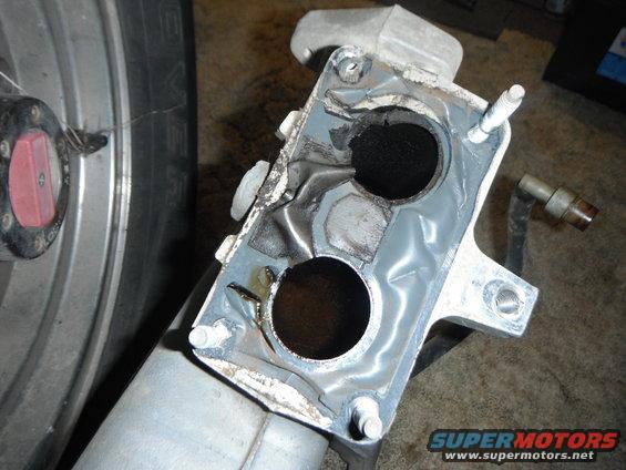 Engine intake manifold with two circular openings, showing signs of wear and gasket material