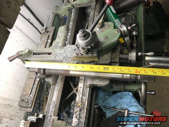 Metal shaft being machined on a lathe, with a yellow measuring tape alongside