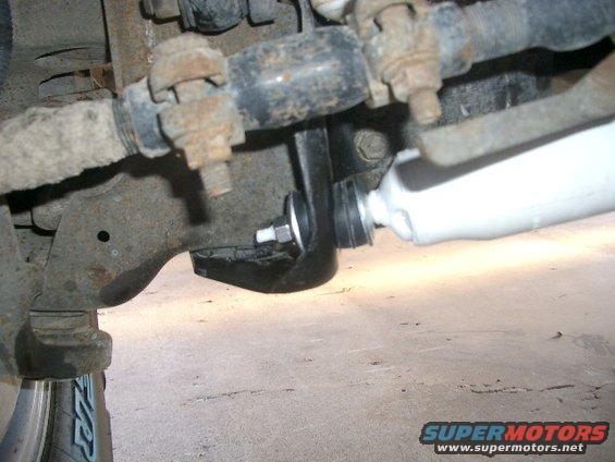 Close-up of a white shock absorber attached to a black bracket and rusty suspension components