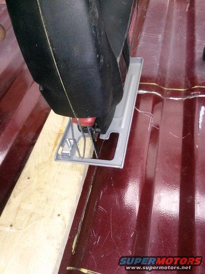 Jigsaw cutting a piece of wood on a dark red, ribbed surface. A Supermotors.net watermark is visible