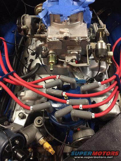 Engine block with carburetor, red spark plug wires numbered 1-8, and blue tape on top