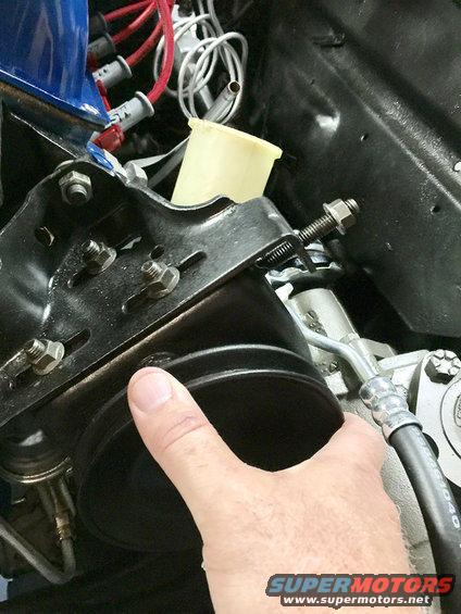Hand pointing to a black engine component with visible bolts and hoses