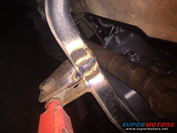 Welded metal frame on a red jack stand, with exhaust pipe and transmission visible