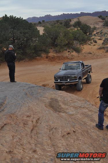 Dark gray Ford F-Series pickup truck with off-road tires driving on a dirt path