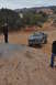 1991 Ford Bronco - A dark gray Ford F-Series pickup truck navigates a rocky, off-road trail with two people observing.