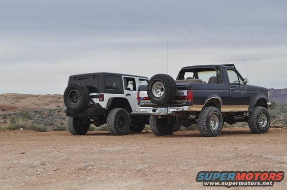 1991 Ford Bronco and a Jeep Wrangler parked on dirt road, rear view