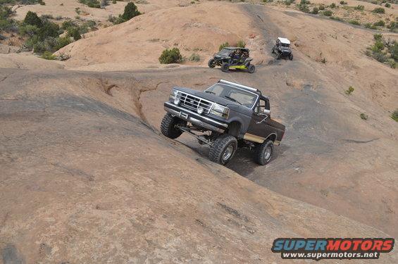Dark gray lifted 1992 Ford F-150 off-roading on rocky terrain with other vehicles