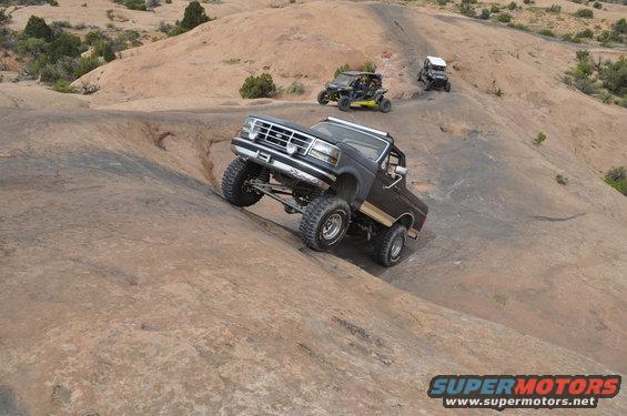 1991 Ford Bronco climbing a steep rock formation with two other off-road vehicles behind it