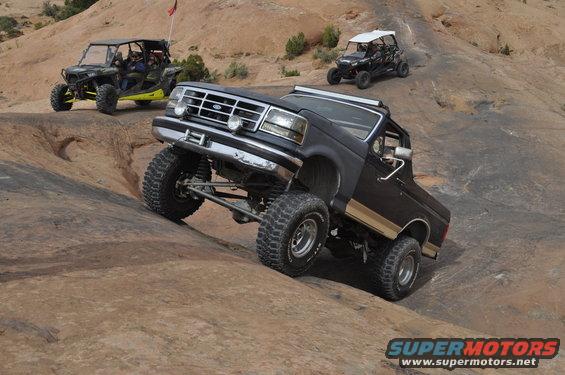 Black Ford Bronco climbing rocky terrain with two UTVs behind it