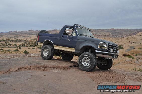 Dark blue Ford Bronco with tan stripe and off-road tires parked on a rocky desert landscape