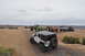 1991 Ford Bronco - A group of modified off-road vehicles traverses a sandy trail in a desert landscape.