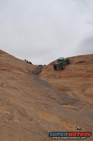Green off-road buggy climbing a rocky incline with people watching