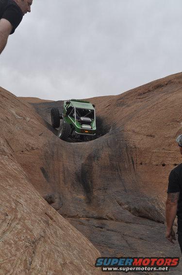 Green off-road buggy climbing a steep rock face in Moab