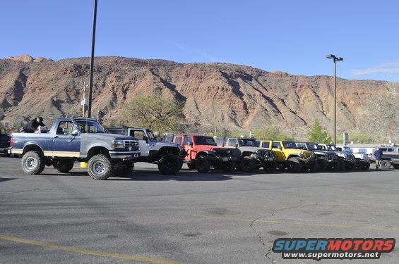 Blue and silver Ford Bronco with lifted suspension and off-road tires, parked in a lot with other vehicles