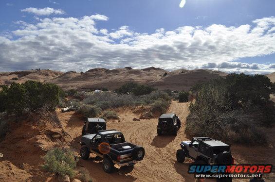 1991 Ford Bronco and other off-road vehicles driving on a sandy trail in a desert landscape