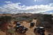 1991 Ford Bronco - Several off-road vehicles navigate a dusty trail through a desert canyon under a cloudy sky.