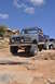 1991 Ford Bronco - This lifted Ford Bronco navigates a challenging rocky trail under a bright blue sky.