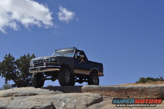 Dark blue lifted 1991 Ford Bronco on rocky terrain under a blue sky