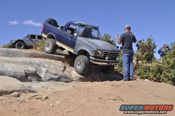 Blue and gray Ford Bronco off-roading on rocks, front grille visible