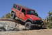 1991 Ford Bronco - A red Jeep Wrangler navigates a challenging rocky trail under a clear blue sky.