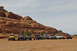 1991 Ford Bronco - A group of Jeeps are lined up in a desert environment with large red rock formations under a cloudy sky.