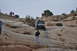 1991 Ford Bronco - A Jeep Wrangler navigates a steep, rocky incline in a desert landscape, observed by onlookers.