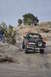 1991 Ford Bronco - A dark blue Ford Bronco navigates a steep, rocky incline with a spare tire mounted on the back.