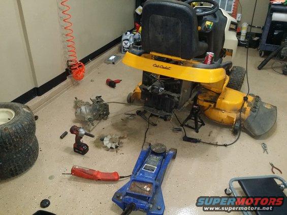 Cub Cadet lawn tractor disassembled on garage floor with tools and parts scattered around