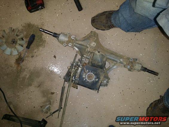 lawn mower transaxle on concrete floor with a screwdriver and fan blade nearby