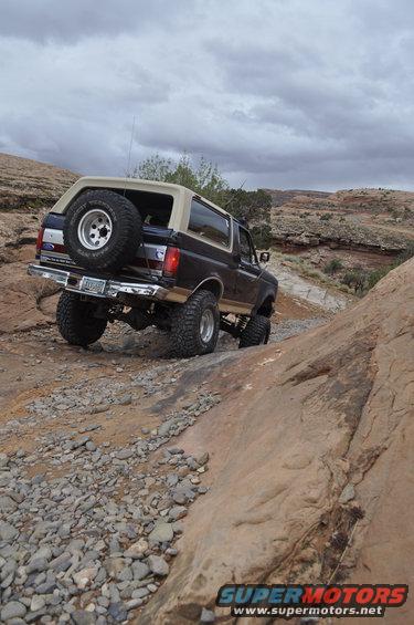 1991 Ford Bronco climbing a rocky desert trail under a cloudy sky
