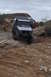 1991 Ford Bronco - Two Jeeps and a red vehicle navigate a challenging off-road trail with rocky terrain and a cloudy sky.