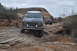 1991 Ford Bronco - A dark gray Ford Bronco with a roof rack drives on a challenging rocky trail, with a red Jeep following behind.