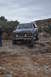 1991 Ford Bronco - A Ford Bronco navigates a rocky off-road trail under a cloudy sky.